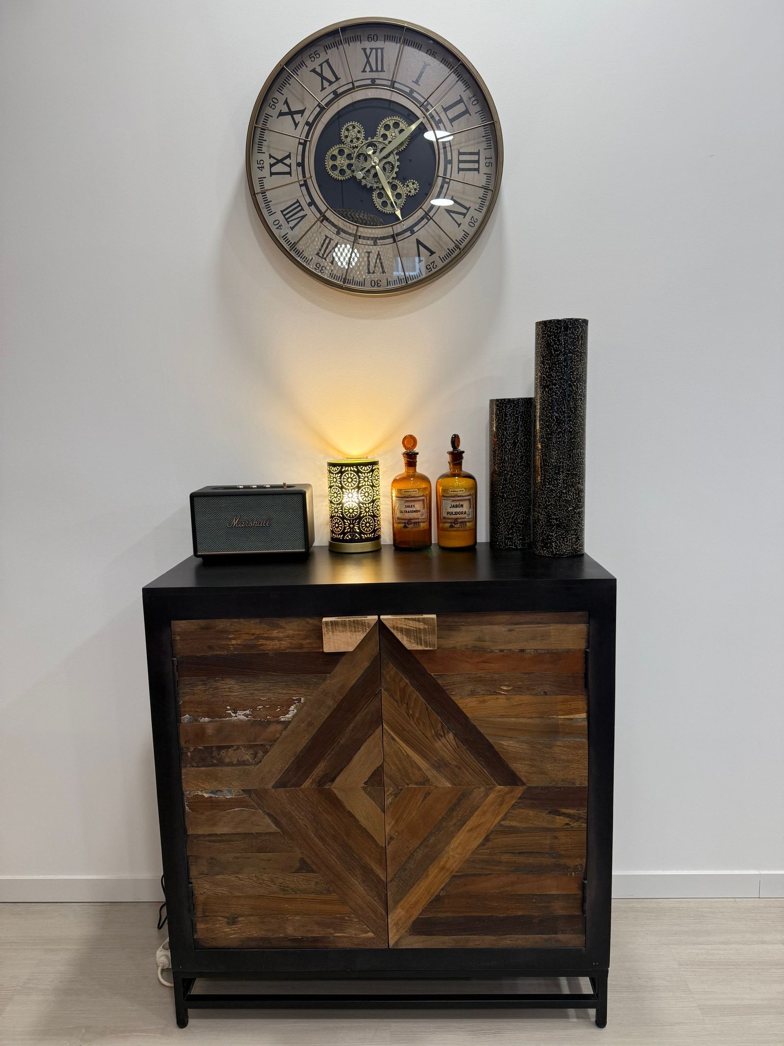 Mueble con puerta geométrica de madera, rematado con decoración y reloj sobre pared blanca.