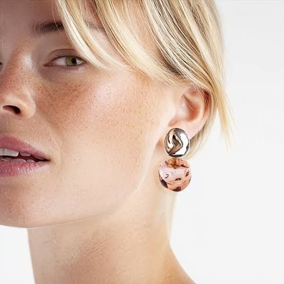 Mujer rubia con pendientes de plata y rosa, mirando fuera de cámara.