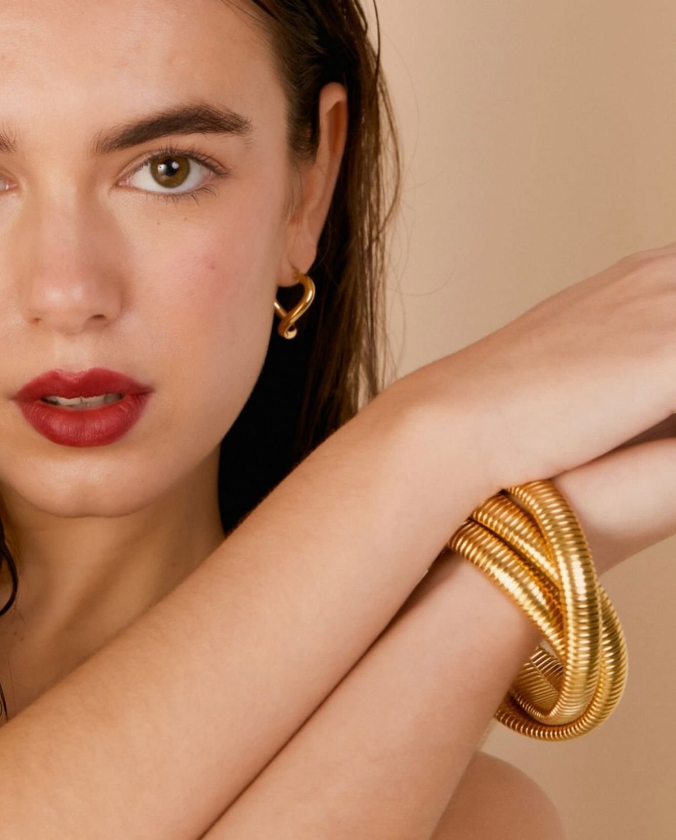 Mujer que lleva pendientes de corazón de oro y una pulsera gruesa de oro.